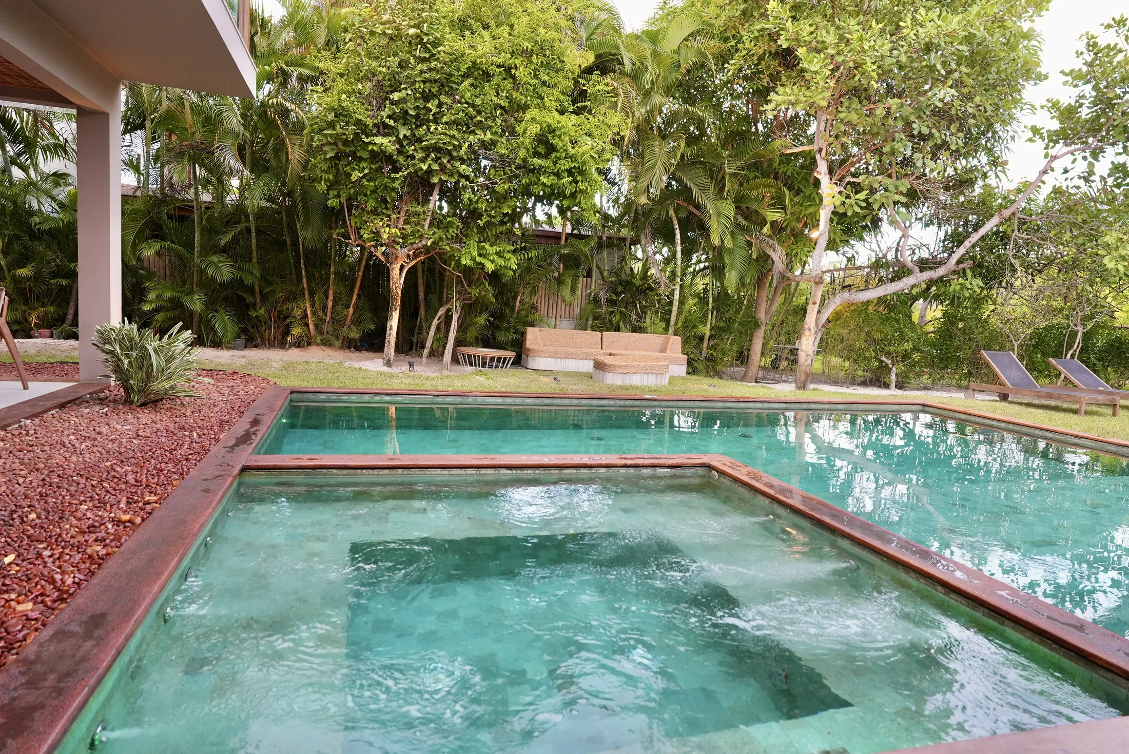 Piscina com jacuzzi e deck de pedra vermelha, entre a vegetação
