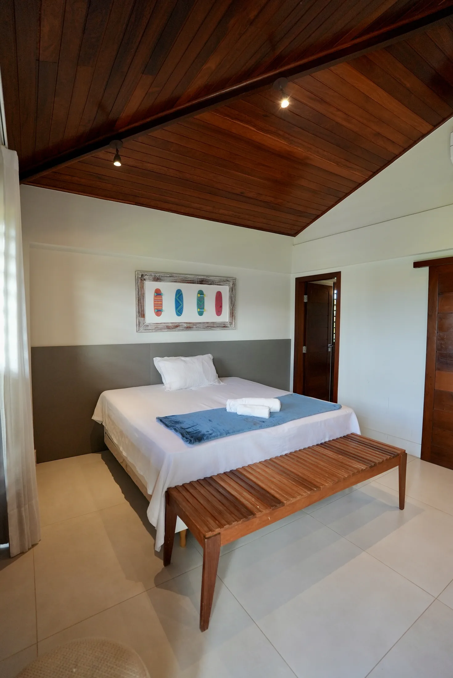 Quarto com cama de solteiro, banco de madeira e pé-direito alto