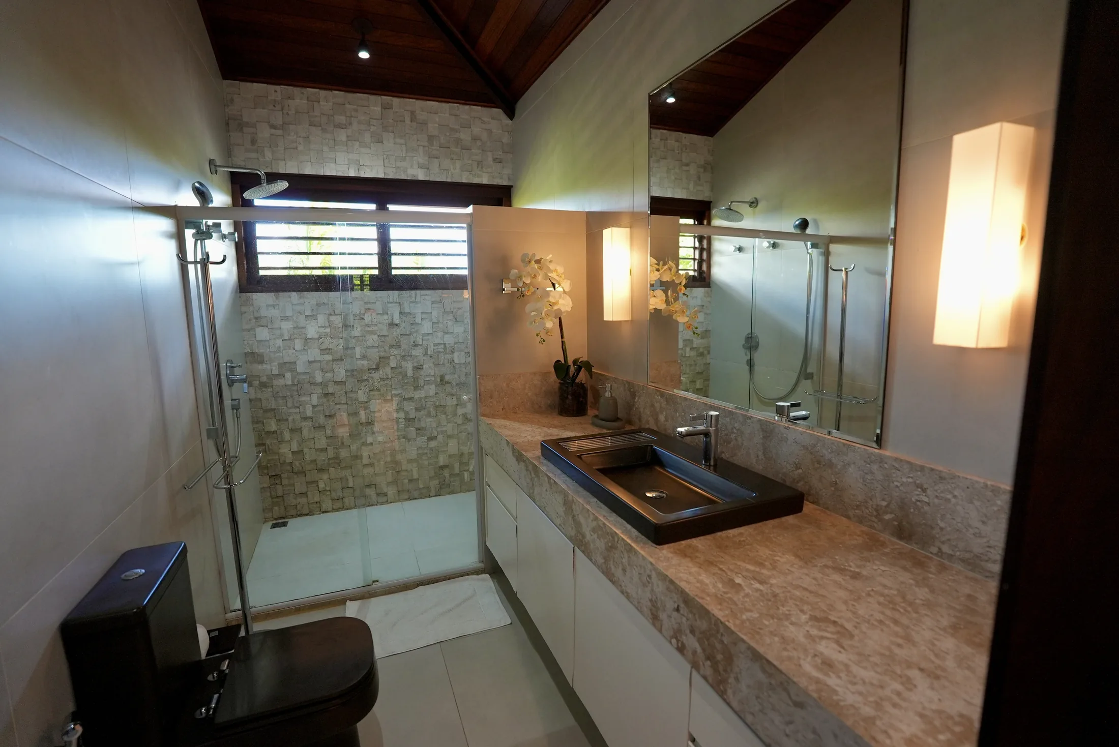 Banheiro com parede de pastilhas, ducha e bancada iluminada